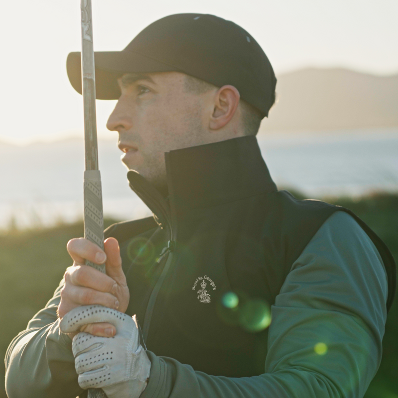 A golfer wearing a Royal St Georges jacket watches his shot